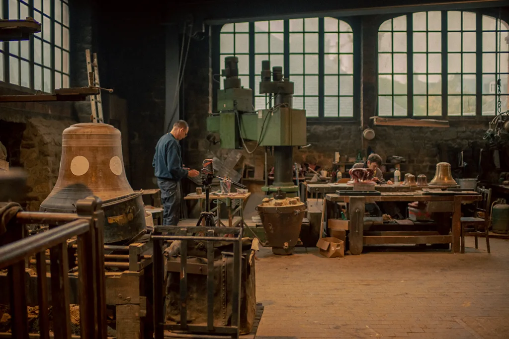 L’atelier de la fonderie Cornille-Havard. L’artiste Vincent Olinet (à gauche de la photo) réalise les décors sur la fausse cloche Julie. (© Tomasz Namerla/Abbaye royale de Fontevraud)