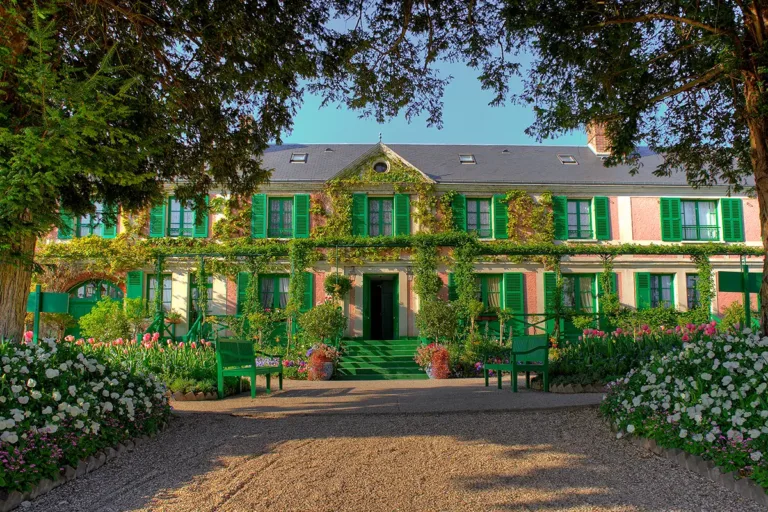La maison du Clos normand. De part et d’autre de l’allée, les deux ifs préservés par Alice Hoschedé. Sur la façade, des rosiers. Le Mermaid, rosier favori de Monet, portait ses fleurs jaunes en offrande jusqu’à la fenêtre de sa chambre. (© Fondation Claude Monet)