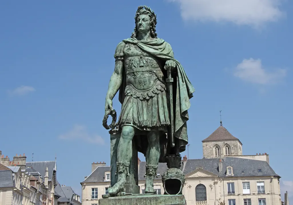 Louis XIV en empereur romain semble avoir toujours dominé la place Saint-Sauveur de Caen. En réalité, cette statue se trouvait depuis le 24 avril 1828 place Royale, devenue en 1883 place de la République ; cette année-là, on enlève l’œuvre pour la remplacer par… un kiosque à mu­sique ! Une première statue du Roi-Soleil sur cette même place avait été décidée en 1684 ; cette sculpture en pierre signée du Caennais Jean Postel est renversée et brisée pendant la Terreur, de sorte que le conseil municipal vote par délibération du 21 décembre 1819 le remplacement (cette fois-ci en bronze) de l’effigie de Louis-le-Grand, qui avait visité Caen le 5 septembre 1685, « cette ville connue pour son dévouement à ses Rois ». On confie la tâche au Parisien Louis-Messidor-Lebon Petitot, dit Louis Petitot, ancien pensionnaire du roi à l’académie de France, auteur de nombreuses œuvres académiques ou allégoriques, dont trois statues de Louis XIV. Sa composition générale, nous apprend le procès-verbal d’inauguration, a été déterminée d’après le choix fait entre divers projets de l’artiste par une commission de l’Institut, à laquelle le corps municipal en avait référé. Suivant l’intention qui a présidé à cette composition, la statue représente le monarque au moment où, rentré triomphant en France, il s’occupe du bonheur et de la gloire intérieure de son royaume par les encouragements qu’il donne aux sciences, aux arts et au commerce. En septembre 1827, pendant les travaux, la dauphine Marie-Charlotte passe à Caen où elle scelle « solennellement de sa main le bloc de marbre qui couronne le piédestal ». (Photo Rodolphe Corbin © Patrimoine Normand)